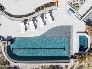 a pool in arizona at desert mountain club that is shaped like a piano surrounded by off-white pavers