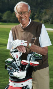 profile shot of jim flick standing next to his golf clubs