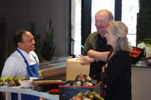 a chef in a white top with a blue apron talking with members at desert mountain club