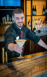 kris vickrey wearing all black with a red tie showing off one of his favorite holiday dishes, serving the autumns apple cocktail at desert mountain club
