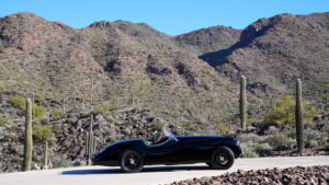 one of the many classic cars in Arizona, a 1953 Jaguar XK120 Supersports Roadster sitting in a driveway with cacti and mountains in the background at desert mountain club