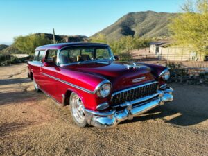 a bright red 1955 Chevy Nomad Restomod sitting on a dirt drive with mountains and bright yellow bushes and trees in the background at desert mountain club