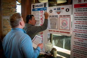 a man writing a calligraphy number on a golf scoreboard as another man with a piece of paper watches closely