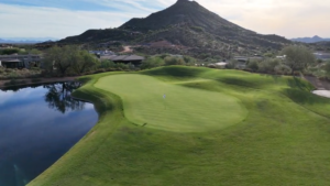 a green at geronimo golf golf course with a green side pond on the left and lone mountain in the background